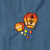 Close-up of blue bag with two embroidered lantern motifs in orange, yellow, cream, and brown, plus small matching embroidered dots below.