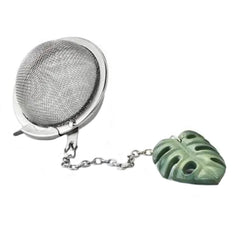 A stainless steel tea infuser ball attached to a green monstera leaf charm